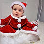 baby, child, santa_hat, christmas_outfit, red_clothing, white_fur_trim, bed, floral_bedspread, indoors, window, curious, cute, holiday, festive, tulle_skirt, person, portrait, holiday_costume, celebration, smiling