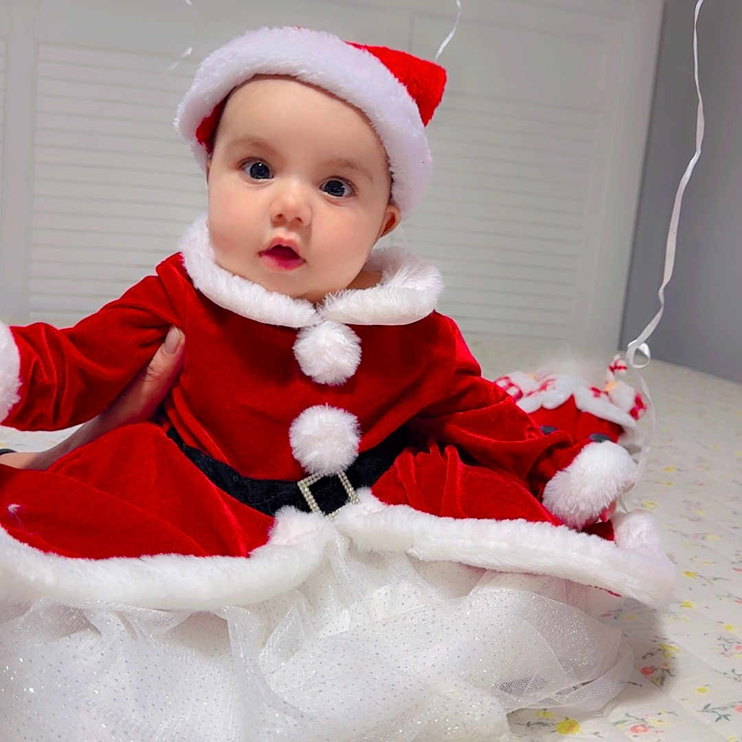 Parry joined the competition — help win amazing prizes! baby, bed, celebration, child, christmas_outfit, curious, cute, festive, floral_bedspread, holiday, holiday_costume, indoors, person, portrait, red_clothing, santa_hat, smiling, tulle_skirt, white_fur_trim, window