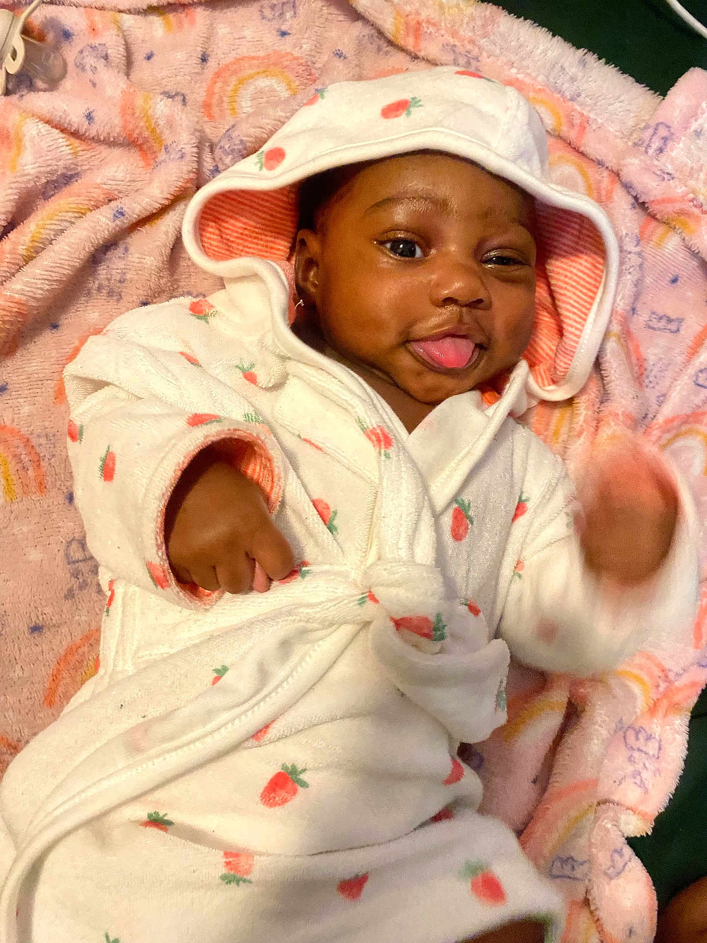 Kaycee joined the competition — help win amazing prizes! baby, child, infant, hooded_robe, strawberry_print, blanket, rainbow_pattern, playful, tongue_out, smiling, cute, soft_texture, lying_down, hand_motion, indoors, cozy, warm_clothing, portrait, young_child, expression