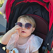 Leïya participe au concours pour gagner de l'argent avec cette photo : accessory, baby, child, clothing, cute, face, hand, happy, infant, outdoor, person, pink_dress, seat, shade, stroller, stuffed_animal, summer, sunglasses, sunlight, toy