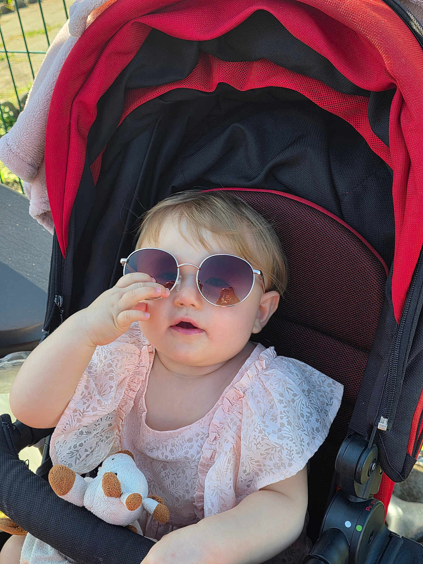Leïya participe au concours pour gagner de l'argent avec cette photo : accessory, baby, child, clothing, cute, face, hand, happy, infant, outdoor, person, pink_dress, seat, shade, stroller, stuffed_animal, summer, sunglasses, sunlight, toy