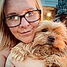 woman, dog, pet, portrait, selfie, glasses, smiling, fluffy, small_dog, cuddling, indoors, warm_lighting, gargoyle, statue, background, closeup, blonde_hair, nose_ring, home, companionship