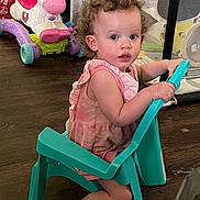Zuri joined the competition — help win amazing prizes! toddler, child, curly_hair, pink_dress, plastic_chair, toy_unicorn, playpen, wooden_floor, indoor, barefoot, holding, seated, furniture, colorful, young_child, cute, curious, play_area, home, girl