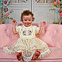 Zuri is registered to the contest to win money with this photo: toddler, child, smiling, curly_hair, lace_dress, pink_couch, easter_eggs, decorations, indoor, portrait, happy, barefoot, playful, seated, cute, celebration, holiday, festive, background, white_door