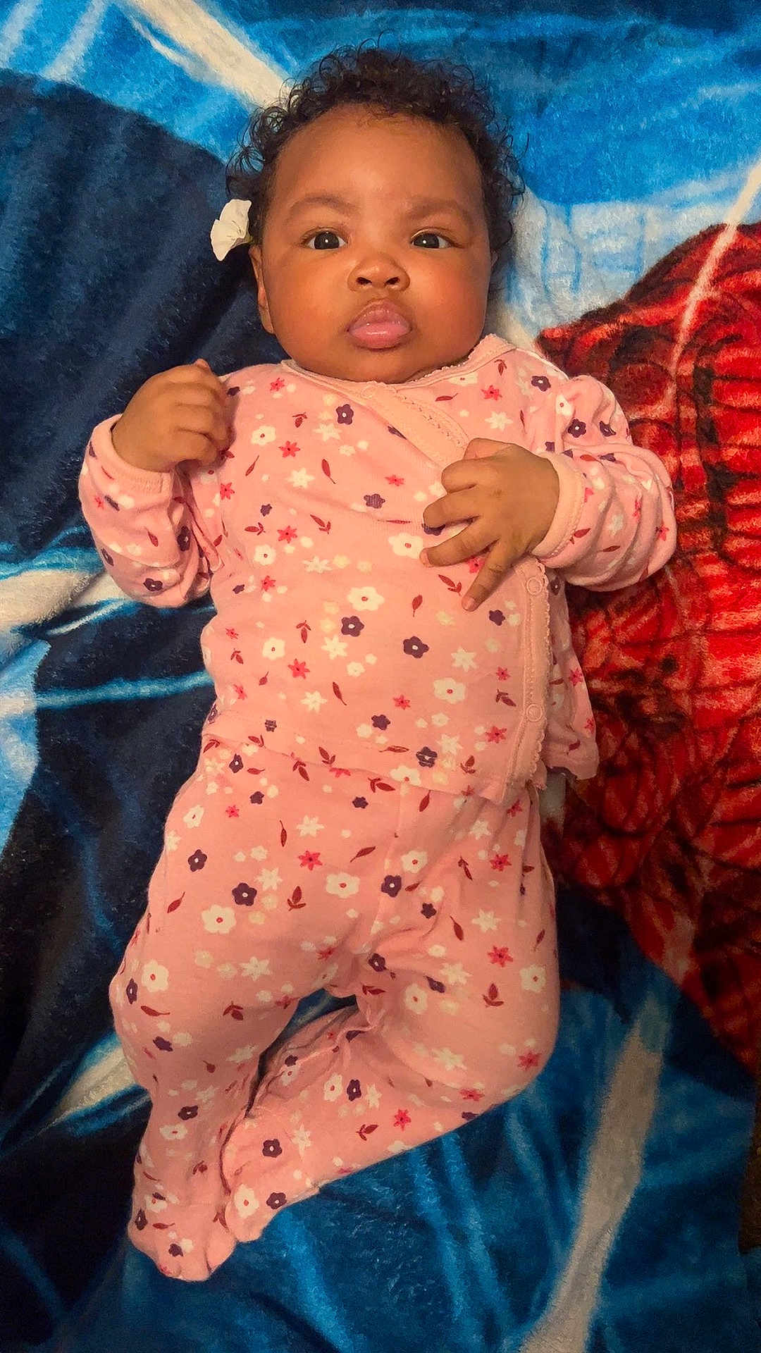 Kinnlaya is registered to the contest to win money with this photo: baby, infant, child, pajamas, pink_clothing, floral_pattern, curly_hair, blanket, blue_blanket, red_blanket, lying_down, indoors, cute, face, hands, footed_pajamas, adorable, portrait, young_child, cozy
