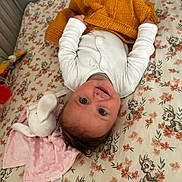 Alice joined the competition — help win amazing prizes! baby, infant, blanket, plush_toy, bed, floral_pattern, smiling, white_clothing, yellow_blanket, lying_down, cute, child, soft_toy, pink_blanket, indoors, head, face, person, happy, cozy