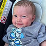 Saylor joined the competition — help win amazing prizes! baby, smile, face, infant, clothing, car_seat, cushion, warning_label, blue, gray_shirt, cute, child, portrait, happy, skin, head, young_child, sitting, indoors, closeup