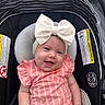 baby, child, smiling, car_seat, bow, headband, pink_clothing, striped, infant, cute, happy, portrait, sitting, indoor, safety, car_seat_warning, clothing, person, young_child, infant_fashion