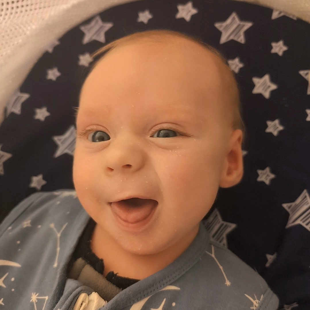 Jace is registered to the contest to win money with this photo: accessories, baby, babylaughing, bed, bodypart, clothing, coat, face, furniture, happy, head, jacket, jewelry, laughing, necklace, newborn, person, photography, portrait, smile