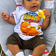 Adriel joined the competition — help win amazing prizes! baby, child, infant, outdoor, grass, baby_seat, toy, banana_toy, garfield_tshirt, white_socks, shorts, cute, smiling, portrait, young_child, casual_clothing, colorful, playful, relaxed, person