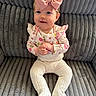 baby, child, infant, pink_bow, floral_top, white_tights, smiling, sitting, couch, plush_fabric, indoor, cute, portrait, hands_clasped, headband, young_child, happy, person, cozy, texture