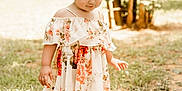Trinity is registered to the contest to win money with this photo: toddler, child, girl, barefoot, floral_dress, outdoor, nature, grass, dirt, sunlight, trees, curly_hair, pink_bow, portrait, young_child, summer, casual_clothing, innocence, daylight, cute