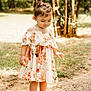 toddler, child, girl, barefoot, floral_dress, outdoor, nature, grass, dirt, sunlight, trees, curly_hair, pink_bow, portrait, young_child, summer, casual_clothing, innocence, daylight, cute