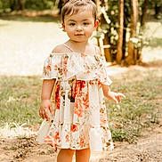 Trinity is registered to the contest to win money with this photo: toddler, child, barefoot, floral_dress, outdoor, nature, grass, trees, sunlight, portrait, young_child, cute, person, standing, hair_tie, dirt_path, daylight, smiling, fashion, casual