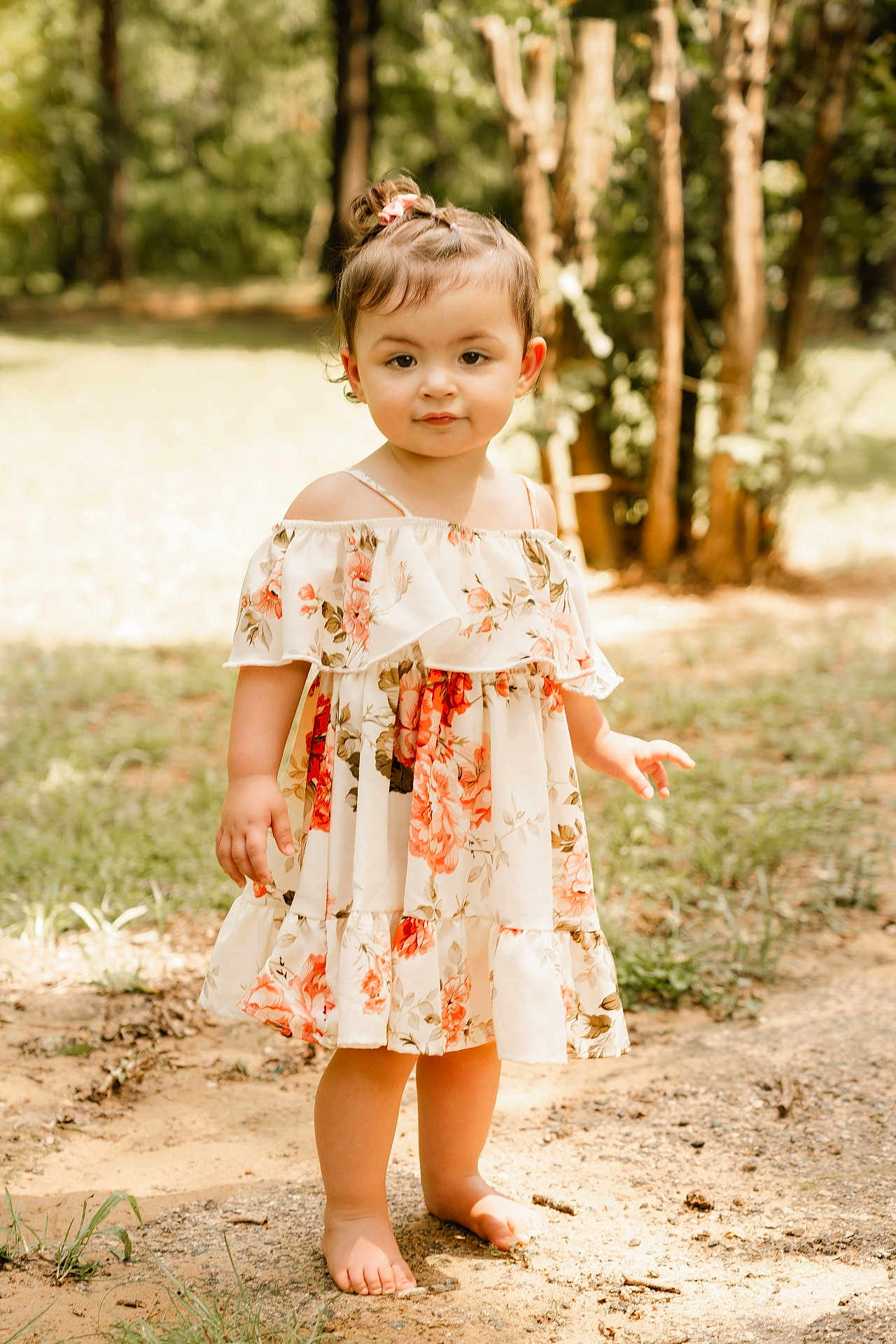 Trinity is registered to the contest to win money with this photo: toddler, child, barefoot, floral_dress, outdoor, nature, grass, trees, sunlight, portrait, young_child, cute, person, standing, hair_tie, dirt_path, daylight, smiling, fashion, casual