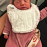 newborn, baby, infant, sleeping, pink_onesie, bib, hand, person, indoor, cozy, soft_texture, portrait, child, cute, peaceful, human, young, clothing, resting, holding