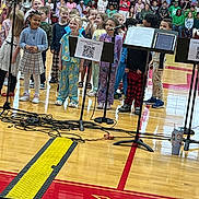 Kinzley joined the competition — help win amazing prizes! audience, bleachers, cables, casual_clothing, children, concert, diverse, floor, group, gymnasium, indoor, kids, microphones, music_stands, pajamas, performance, school_event, smiling, wood_floor, young