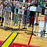 children, kids, gymnasium, microphones, music_stands, concert, pajamas, audience, bleachers, floor, school_event, performance, smiling, group, indoor, wood_floor, cables, diverse, casual_clothing, young