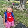 Kinzley is registered to the contest to win money with this photo: child, girl, smile, backpack, red_dress, braided_hair, outdoor, sidewalk, tree, grass, playground, tricycle, sunlight, happy, casual_clothing, nature, summer, play, portrait, cute