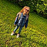 Sophia is registered to the contest to win money with this photo: child, curly_hair, heart_sunglasses, denim_jacket, backpack, jeans, sneakers, grass, outdoor, sunlight, greenery, smile, happy, person, standing, nature, casual_clothing, playful, young, portrait