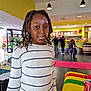 child, girl, face_paint, glitter, indoors, cafe, people, sweater, striped_clothing, dreadlocks, table, can, yellow_wall, lighting, portrait, casual, smile, decor, background, event