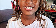 Jahlyss participe au concours pour gagner de l'argent avec cette photo : child, smiling, glasses, dreadlocks, tshirt, sitting, couch, living_room, portrait, happy, indoor, person, bracelet, furniture, home, decor, television, art, casual, young