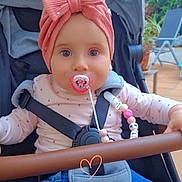 Elsa a rejoint le concours — aidez-le/la à gagner de superbes lots ! baby, child, stroller, pacifier, headband, pink_bow, outdoor, plants, patio, clothing, blue_jeans, beaded_clip, seatbelt, happy, face, person, cute, smile, toy, heart_doodle