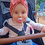 baby, child, stroller, pacifier, headband, pink_bow, outdoor, plants, patio, clothing, blue_jeans, beaded_clip, seatbelt, happy, face, person, cute, smile, toy, heart_doodle