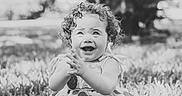 Ava is registered to the contest to win money with this photo: toddler, child, curly_hair, smiling, barefoot, grass, outdoor, dress, happy, clapping, nature, portrait, sitting, daylight, baby, playful, cute, young_child, expression, joyful