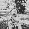 toddler, child, curly_hair, smiling, barefoot, grass, outdoor, dress, happy, clapping, nature, portrait, sitting, daylight, baby, playful, cute, young_child, expression, joyful