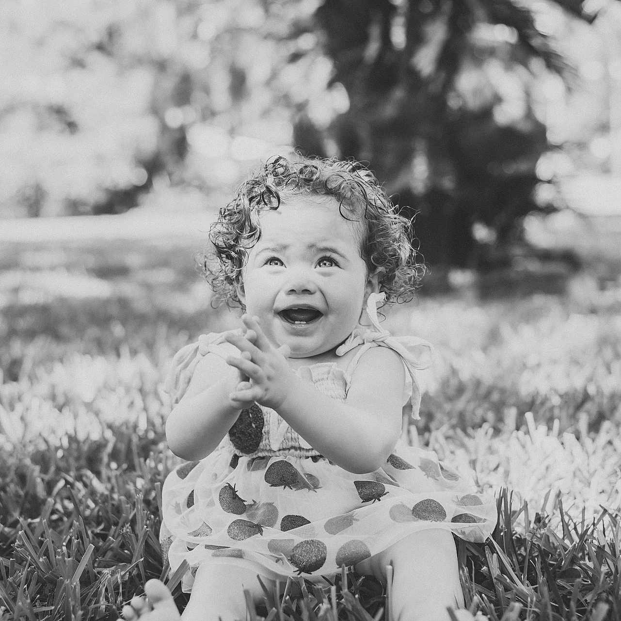 Ava is registered to the contest to win money with this photo: toddler, child, curly_hair, smiling, barefoot, grass, outdoor, dress, happy, clapping, nature, portrait, sitting, daylight, baby, playful, cute, young_child, expression, joyful