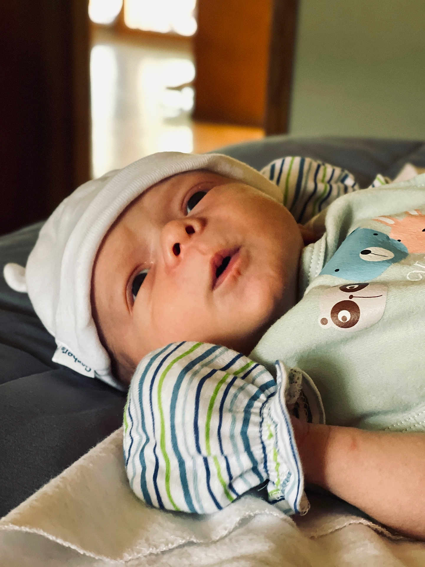 Enzo joined the competition — help win amazing prizes! baby, infant, hat, striped_clothing, blanket, closeup, face, person, cute, sleepwear, lying_down, soft_lighting, indoors, newborn, portrait, apparel, headwear, expression, skin, child