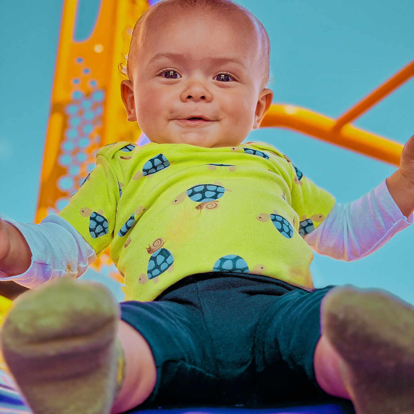 Enzo is registered to the contest to win money with this photo: baby, child, smiling, playground, slide, outdoor, blue_sky, green_shirt, turtle_print, shorts, happy, fun, feet, closeup, person, cute, play, summer, daylight, park