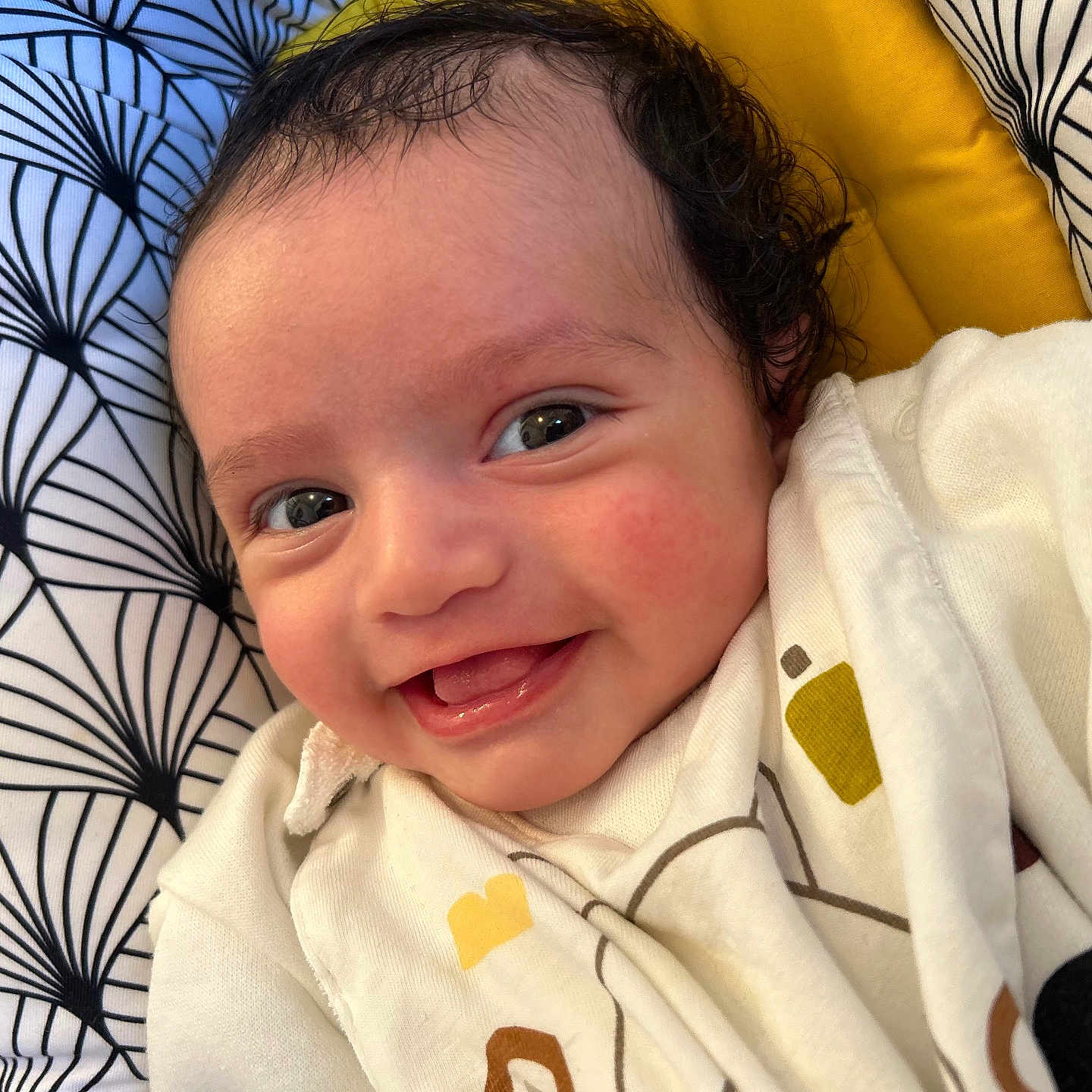 Swan participe au concours pour gagner de l'argent avec cette photo : baby, cheeks, child, closeup, clothing, cozy, curly_hair, cute, eyes, face, happy, indoor, infant, lying_down, patterned_cushion, portrait, skin, smiling, white_outfit, yellow_background