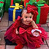 baby, child, red_dress, headband, bow, christmas, presents, gift_boxes, holiday_lights, smile, happy, outdoor, brick_patio, festive, tulle_skirt, red_booties, celebration, cute, person, portrait