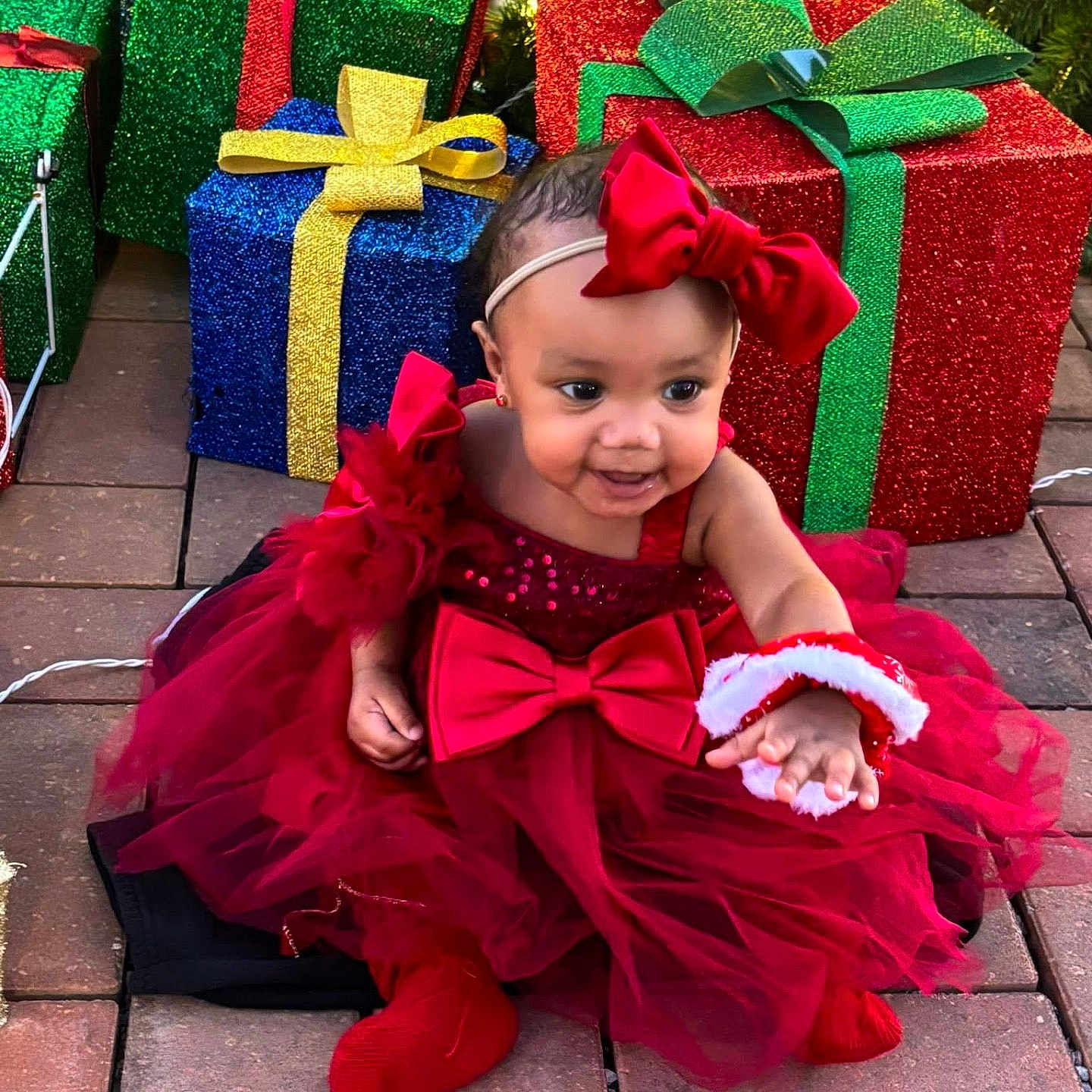 Sariyah joined the competition — help win amazing prizes! baby, child, red_dress, headband, bow, christmas, presents, gift_boxes, holiday_lights, smile, happy, outdoor, brick_patio, festive, tulle_skirt, red_booties, celebration, cute, person, portrait