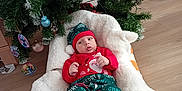 Andrew participe au concours pour gagner de l'argent avec cette photo : baby, infant, christmas_tree, ornament, blanket, holiday_outfit, santa_print, christmas_hat, socks, plush_bed, wooden_floor, pine_branches, decorations, bauble, indoor, newborn, festive, portrait, lying_down, cozy