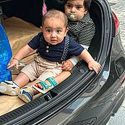 Habeebullah joined the competition — help win amazing prizes! toddler, baby, child, car_trunk, pacifier, striped_clothing, shorts, sneakers, sandals, blue_bag, pavement, curious, sitting, holding, black_car, outdoor, expression, candid, cute, two_children