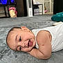 baby, smiling, carpet, infant, lying_down, arm, scratch, white_clothing, indoor, home, floor, face, cheerful, child, person, soft_texture, cute, relaxed, head, closeup