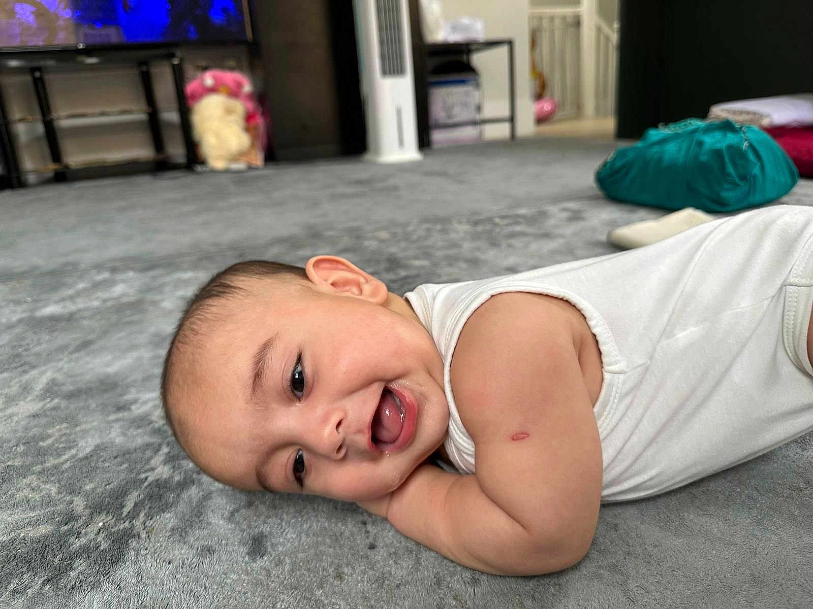 Habeebullah joined the competition — help win amazing prizes! baby, smiling, carpet, infant, lying_down, arm, scratch, white_clothing, indoor, home, floor, face, cheerful, child, person, soft_texture, cute, relaxed, head, closeup
