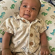 Angel joined the competition — help win amazing prizes! baby, infant, smiling, face, clothing, button_up, pillow, dinosaur_print, cute, indoors, portrait, child, happy, skin, hand, sitting, textile, fabric, hair, person
