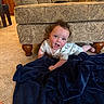 Malachi is registered to the contest to win money with this photo: baby, child, infant, couch, blanket, carpet, floor, indoors, furniture, curly_hair, smiling, playful, face, person, cute, home, legs, blue_blanket, pattern, wooden_leg