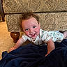 baby, child, couch, carpet, blanket, smile, curly_hair, indoor, furniture, happy, face, person, patterned_fabric, wooden_leg, clothing, infant, floor, cute, playful, home
