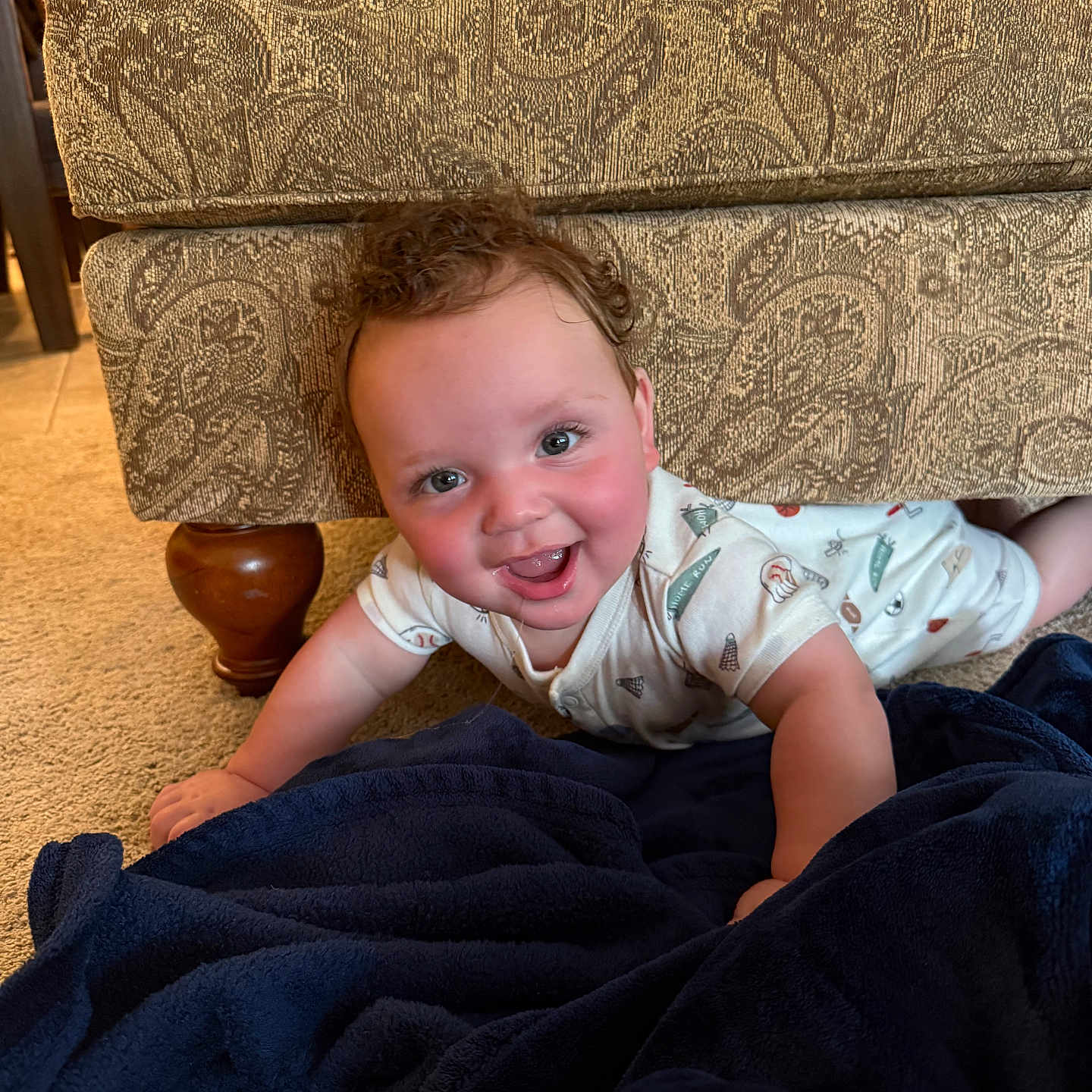 Malachi is registered to the contest to win money with this photo: baby, child, couch, carpet, blanket, smile, curly_hair, indoor, furniture, happy, face, person, patterned_fabric, wooden_leg, clothing, infant, floor, cute, playful, home