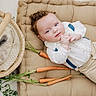 Malachi is registered to the contest to win money with this photo: baby, child, curly_hair, white_shirt, beige_pants, cushion, carrots, basket, bunny, fluffy, soft_texture, cute, indoor, portrait, laying_down, animal, pet, relaxed, adorable, light_background