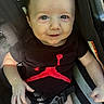 baby, infant, car_seat, smiling, black_onesie, red_graphic, face, eyes, hand, straps, child, cute, seatbelt, clothing, young, portrait, indoors, happy, skin, person