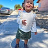 casual_clothing, child, cute, daylight, fashion, green_skirt, hair_buns, happy, outdoor, person, portrait, purple_boots, sidewalk, smiling, standing, sunny, toddler, urban_background, white_sweater, young_child