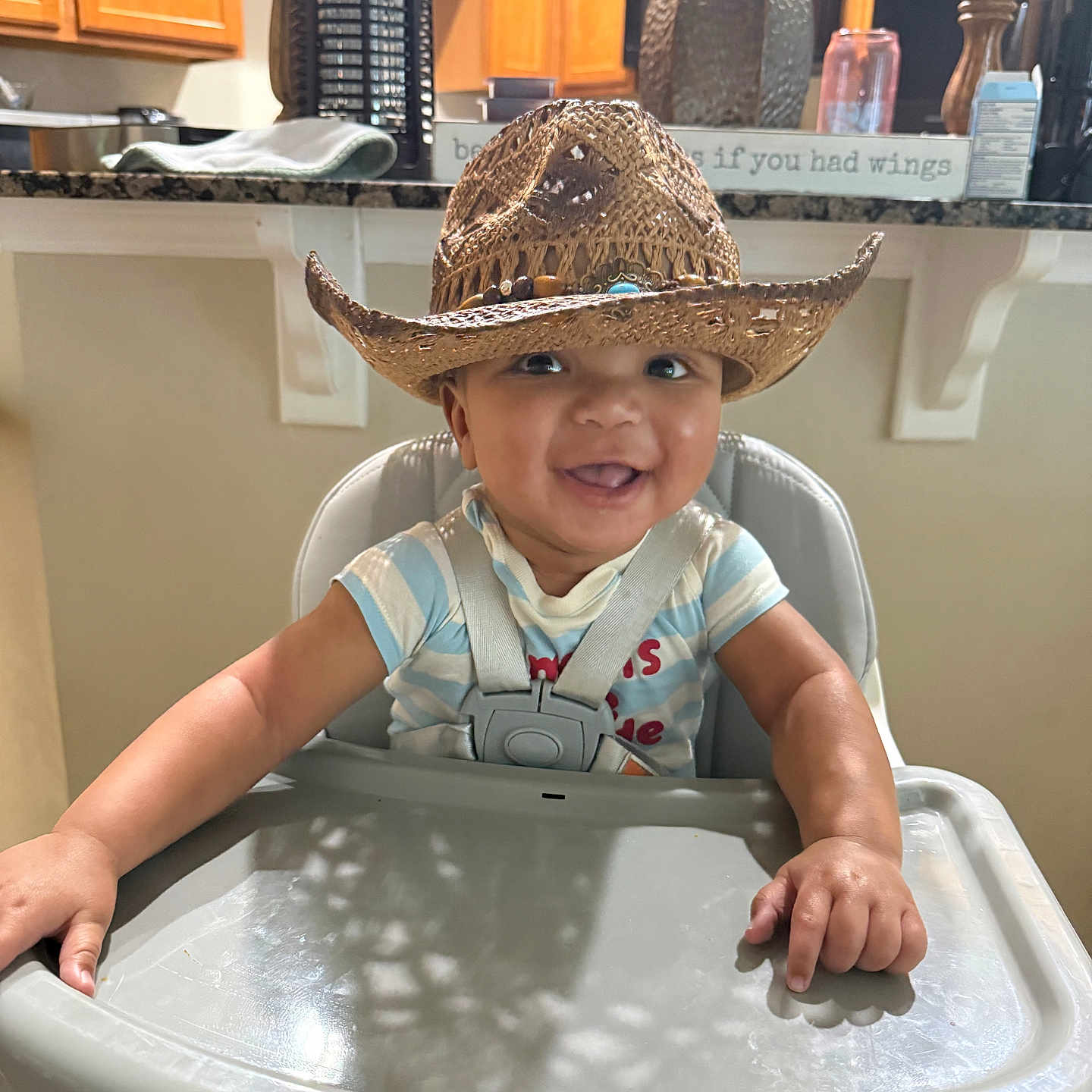 Reshard Mcelroy Jr is registered to the contest to win money with this photo: baby, child, cowboy_hat, high_chair, smile, happy, indoor, kitchen, wooden_cabinets, feeding_chair, infant, person, cute, adorable, straps, table, face, expression, home, decor