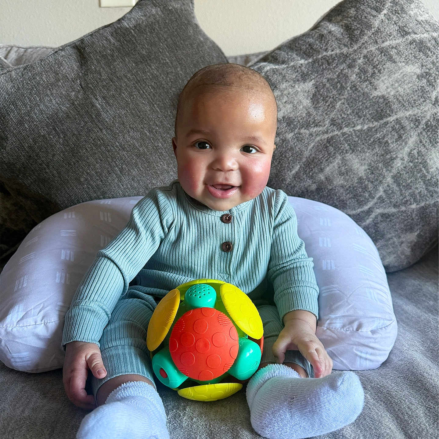 Reshard is registered to the contest to win money with this photo: baby, child, clothing, colorful, comfortable, couch, cute, face, happy, home, indoor, infant, person, pillow, play, portrait, seated, smiling, socks, toy