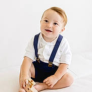 Rocky joined the competition — help win amazing prizes! toddler, child, smiling, white_shirt, navy_suspender, wooden_toy, toy_ship, barefoot, sitting, cross_legged, light_background, indoor, cute, happy, young_child, playful, portrait, innocence, minimalist, baby